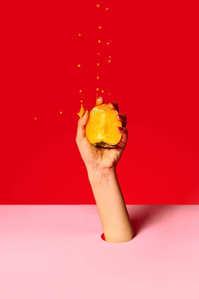 Juicy sweet persimmon. Authentic female hand squeezes half of fruit over pink red background.Pop art food photography. Drops of juice fly up. Concept of healthy eating, art, fashion, ad