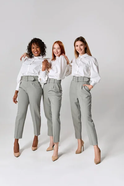 Happy fashionable stylish young women in office style clothes posing over light background. Concept of beauty, fashion, business. Multiethnic fashion models