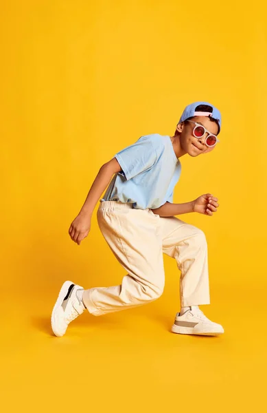 一个充满活力的非洲小男孩的肖像 穿着时尚街道风格衣服的嘻哈舞者在明亮的黄色背景上跳舞 音乐的概念 舞蹈的快乐 小孩看起来很开心 很活泼 — 图库照片