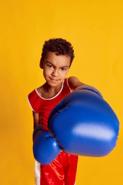 Yumruk. Aktif küçük bir çocuk, spor üniformalı boksör ve sarı arka planda izole edilmiş boks eldivenleri. Spor anlayışı, aktif ve sağlıklı yaşam tarzı, çocuk duyguları. POV