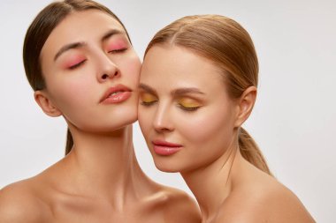 Couple of beautiful sensual young women, blond and brunette with well-kept skin posing over light background. Concept of natural beauty, fashion, skin care and health, ad