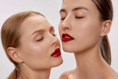 Calmness. Two sensual beautiful young women with nude makeup and red lipstick posing with closed eyes. Concept of love, emotions, beauty, vision, health and fashion