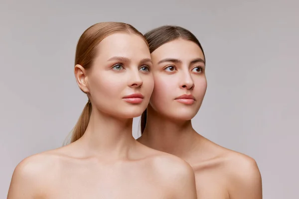 Confidence. Couple of beautiful elegant young women, blond and brunette with well-kept skin posing over light background. Concept of natural beauty, fashion, skin care and health, ad