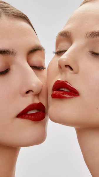 Passion. Vertical cropped portrait of young beautiful female couple. Models with well-kept skin and red lipsticks on lips. Concept of emotions, beauty, vision, health and fashion.