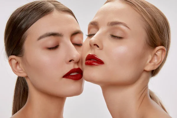 Love. Two sensual beautiful young women with nude makeup and red lipstick posing with closed eyes. Concept of love, emotions, beauty, vision, health and fashion