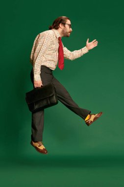 Be late. Portrait of retro mature man with moustache and beard in eyeglasses in vintage fashion jumping clothes over dark green background. Concept of retro style, emotions, business, work