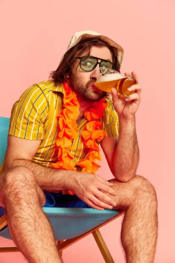 Bira zamanı. Yazlık gömlekli ve göğsünde Hawaii çelengi olan pembe arka planda poz veren biri. Boş zaman aktivitesi, tatil, yaz, dinlenme ve erkek hobileri konsepti