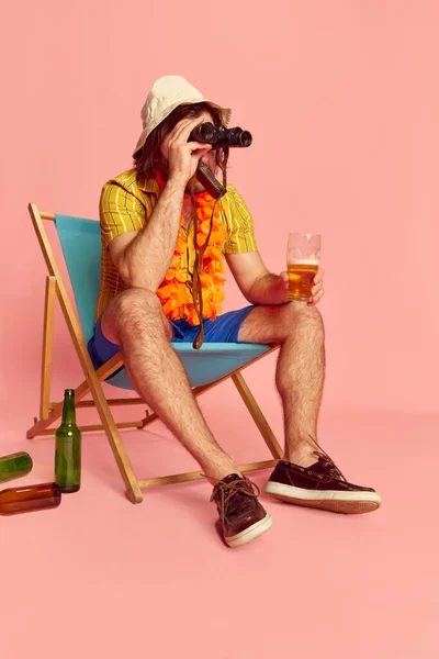 クールなビーチガー 夏のシャツの男とピンクの背景に双眼鏡を通して見て胸にハワイの花のガーランドと短い 余暇活動 休息と男性の趣味の概念 — ストック写真