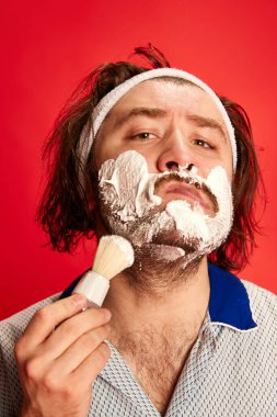 Tıraş. Saç bandı takmış, pijamalı, sakallı, yüzünde köpük olan genç bir adam. Cilt bakımı, kişisel bakım, kozmetik, komik mim duyguları. Yakın plan portre