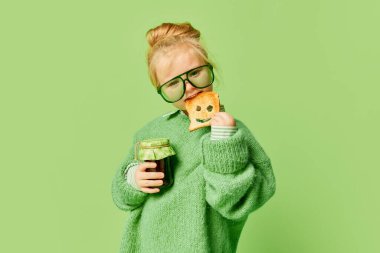 Bir şeyler atıştır. Mutlu gülümseyen şirin çocuk, şık giyinen küçük kız ve açık yeşil arka planda poz veren güneş gözlüğü. Bahar moda koleksiyonu, mutluluk, reklam konsepti. Tek renkli portre