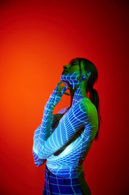 Kırmızı arka planda dijital neon ışıklı genç kadın portresi görüyorum. Sanat, moda, siber punk, fütürizm ve yaratıcılık kavramı. Vücutta projektör ışığı aydınlatması