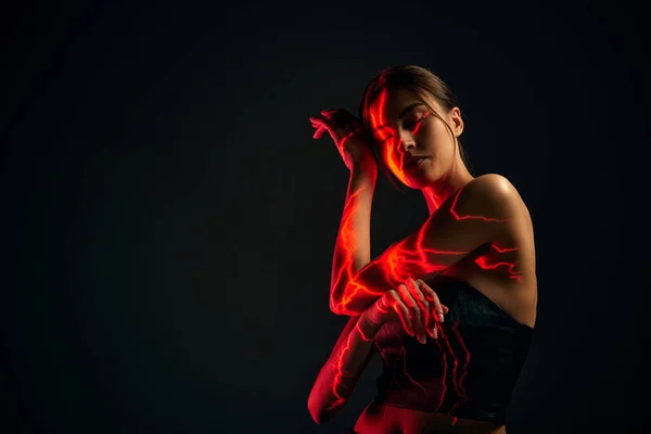 Fire energy. Creative portrait of young sensual woman with digital neon filter lights on body over dark mode background. Concept of digital art, fashion, cyberpunk, futurism and creativity