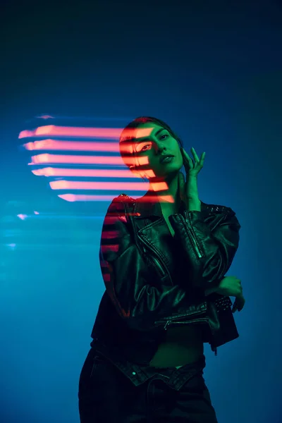 Day and night. Half-length portrait of young stylish woman posing over dark blue background with neon mixed light lines. Concept of contemporary art, fashion, cyberpunk, futurism