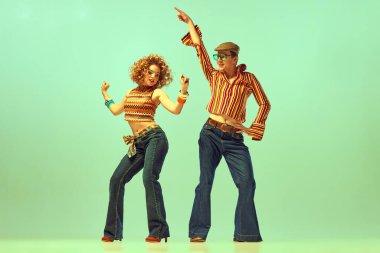 Happy and active dancers. Two excited people, man and woman in retro style clothes dancing disco dance over green background. 1970s, 1980s fashion, music, hippie lifestyle clipart