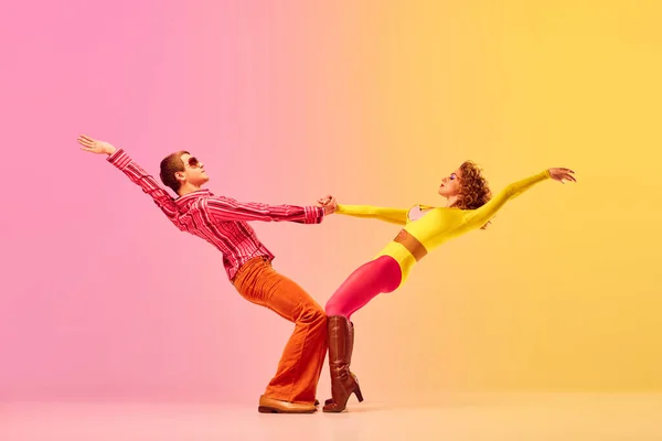 Support. Young stylish emotional man and woman, professional dancers in retro style clothes dancing disco dance over pink-yellow background. 1970s, 1980s fashion, music concept