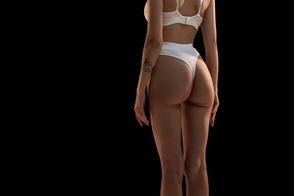 Back view of cropped female body in white inner wear isolated over dark background. Anti-cellulite care cosmetology. Concept of beauty, body care, health, plastic surgery, fashion, cosmetics, spa, ad