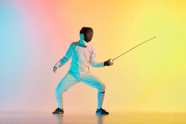 stock image Fencer takes a stand. Young man, male fencer with sword practicing in fencing over gradient pink-yellow background in neon light. Sportsman shows fencing technique. Copyspace for ad.
