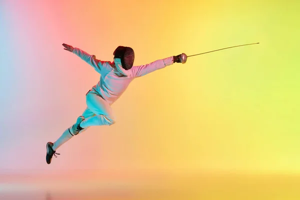 長い攻撃だ 若い男 ネオンの光のグラデーションピンク黄色の背景にフェンシングの剣の練習を持つ男性のフェンシング スポーツマンはフェンシング技術を示しています 広告のコピースペース — ストック写真