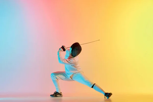 フェンサーは立ち上がる 若い男 ネオンの光のグラデーションピンク黄色の背景にフェンシングの剣の練習を持つ男性のフェンシング スポーツマンはフェンシング技術を示しています 広告のコピースペース — ストック写真
