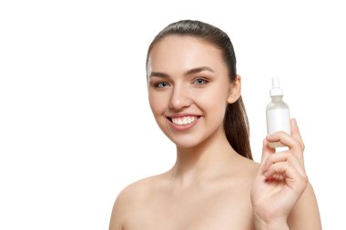 Serum şişesini gösteren bir model. Beyaz arka planda iyi korunmuş cildi olan gülümseyen güzel bir kız. Yüz kozmetik maskeleri. Doğal güzellik kavramı, cilt bakımı, kozmetoloji, sağlık, reklam