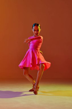 Tek kişilik performans. Stüdyo fotoğrafı, 11 yaşında bir çocuk neon ışıkta kahverengi arka planda balo dansı yapıyor. Güzellik anlayışı, profesyonel danslar.