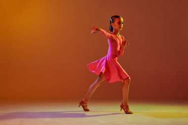 Tek kişilik performans. Stüdyo fotoğrafı, 11 yaşında bir çocuk neon ışıkta kahverengi arka planda balo dansı yapıyor. Güzellik anlayışı, profesyonel danslar.