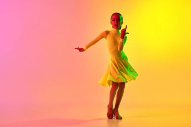 Hareketli müzik. Sarı sahne elbisesi içinde duygusal küçük kız, klasik balo dansını neon ışık filtresiyle, gradyan pembe arka planda yapıyor. Güzellik anlayışı, profesyonel danslar.