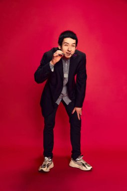 Şüphe, şaşkınlık. Genç bir adamın portresi öne eğiliyor ve kırmızı arkaplanda kameraya bakıyor. Eğitim, öğrenim ve öğrenim hayatı kavramı