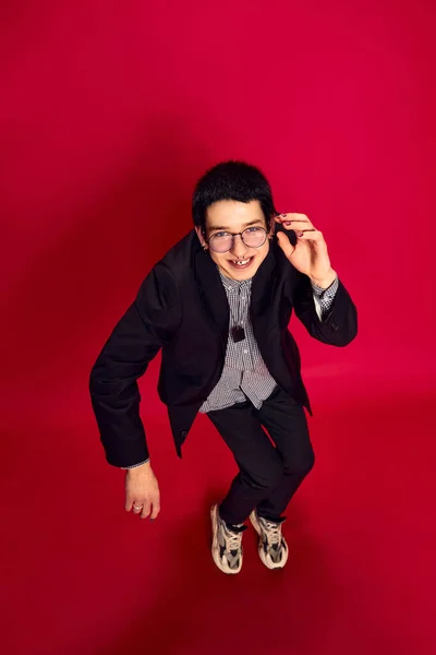 Weird, funny. Portrait of stylish young man with glasses in strange pose over red background. Concept of student life, enjoying life. Looking up. High angle view