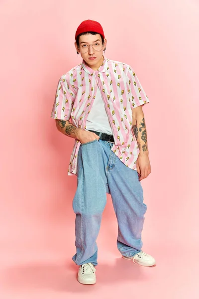 ポケットに手を入れてピンクの背景にカメラを見て入れ墨を持つスタイリッシュな男の肖像画 ファッション 学生生活の概念 — ストック写真
