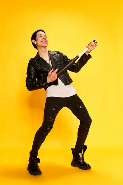 クレイジー 面白い パンク ギターを演奏し 黄色の背景に笑みを浮かべてのような野球バットを持つ若い男 サブカルチャー 学生生活の概念 — ストック写真