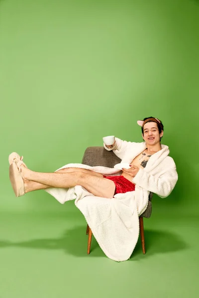 Junger Mann Weiblichem Bademantel Und Hausschuhen Sitzt Auf Einem Stuhl — Stockfoto