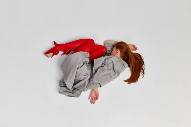 Impersonal human emotions. Stylish girl in grey coat and bright red tights moves over light background. Expressive fashion. Concept of art photography, beauty. Redhaired model in contemporary dance clipart