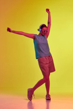 Müzik dinlemek ve dans etmek. Kulaklık takan, müzik dinleyen ve sarı-turuncu arka planda neon ışıkta el ele gezen sevimli bir kız. Müzik anlayışı, gençlik, boş zaman, ruh hali, reklam