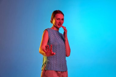 Reddetme, antipati, nefret. Huysuz, suratını buruşturan ve neon ışıkta mavi arka planda iğrenç hareketler yapan genç bir kız. İnsani duygu kavramı, kendini ifade etme, ruh hali, reklam