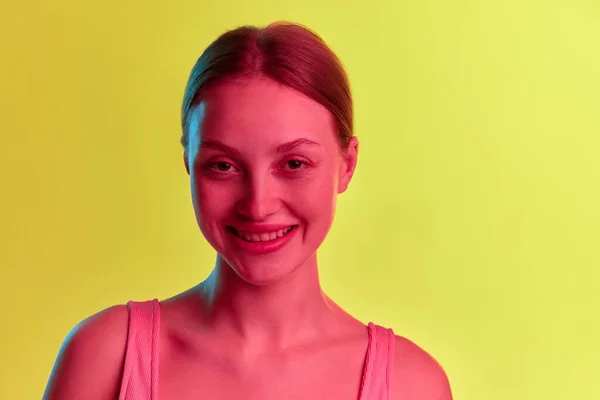 Positive emotions. Happy pretty girl with pleasure face looking up and smiling over yellow-orange background in neon light. Concept of beauty, youth, human emotions, mood, ad