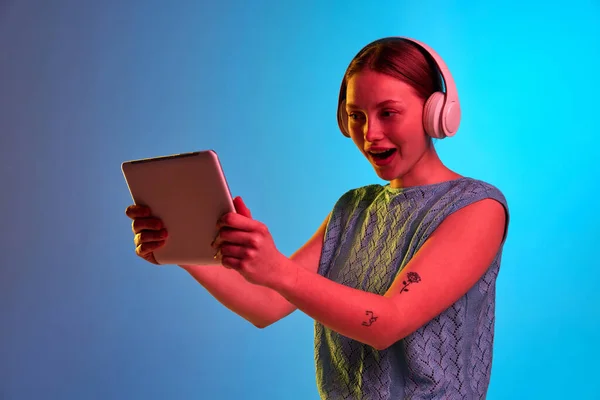 Surprise, exciting. One young adorable girl wearing headphones holding tablet and looking with open mouth and excited facial expression. Concept of human emotions, mood, gadgets, music, chatting, ad