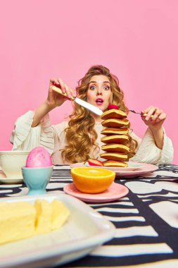 Yiyeceğin büyük bir kısmı. Uzun kıvırcık saçlı güzel bir kadın pembe arka planda kocaman bir porsiyon krep yiyor. Sabah konsepti, kahvaltı, retro, vintage, ad