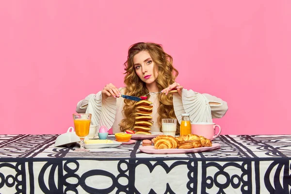 Remember good manners. One charming woman gracefully holding cutlery and tasting pancakes over pink background. Concept of morning, food, breakfast, retro, vintage, etiquette
