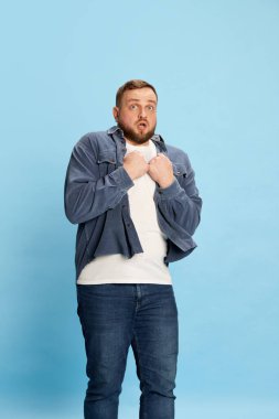 Korkak mavi gözler. Yakışıklı adam ayakta duruyor ve mavi arka planda korku dolu yüz ifadeleriyle ellerini göğsüne koyuyor. Parlak duygular kavramı, yüz ifadesi, ruh hali, reklam