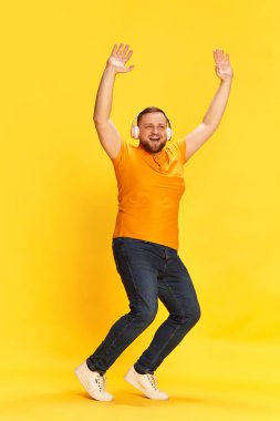 Neşe, müzik, mutluluk, gülümseme. Gülümseyen bir adam sarı arka planda eğlenen bir yüzle müziğe atlıyor. Parlak duygular, hobi, yüz ifadesi, ruh hali kavramı