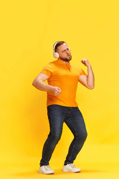 最喜欢的旋律 令人兴奋的是 男人戴着耳机 一边听音乐 一边在黄色的背景上手舞足蹈 业余爱好 人类情感 广告的概念 — 图库照片