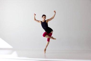 Zarafet gösteriyorum. Sivri uçlu ayakkabılar giyen, dans eden ve beyaz arka plana bakan sevimli balerin. Klasik bale kavramı, ilham, güzellik, dans, yaratıcılık