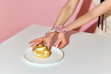 Ölçüm bandı. Pembe arka planda pastayı götüren koli bandıyla bağlanmış kadın ellerinin kırpılmış görüntüsü. Diyet, gıda bağımlılığı, güzellik, abur cubur, aldatma, yeme bozukluğu kavramı