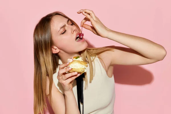 樱桃在蛋糕上 一个漂亮的模特在粉色背景下愉快地吃蛋糕 欺骗餐 饮食崩溃 强迫性的暴食观念 暴食症 模范生意 — 图库照片
