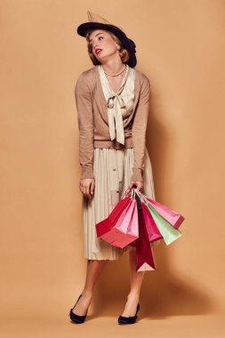 Zor bir alışveriş. Eski giysiler giyen yorgun, güzel bir kadın bej arka planda rahatsız edici yüz ifadesi olan yeni alışverişler yapıyor. Konsept duygular, güzellik, moda, retro stil, vintage, 60 'lar