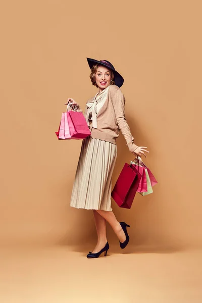 stock image Shopping can cheer. Attractive woman wearing vintage old clothes and holding paper bags over beige background. Concept human emotions, beauty, fashion, retro style, vintage, 60s and Black Friday