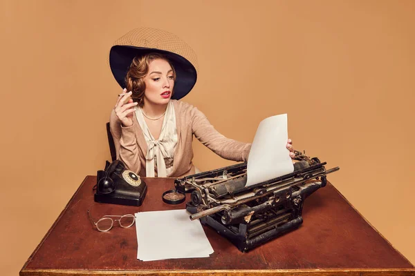 Thoughts, ideas. Beautiful woman writer sitting at typewriter smoking and reading poems over beige background. Concept poems, novel, emotions, beauty, fashion, retro style, vintage