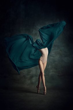 Açık kanatlar. Koyu yeşil arka planda izole edilmiş kumaşla bej bir kıyafetle dans eden hassas profesyonel balerin pozu. Klasik bale kavramı, ilham, güzellik, dans, yaratıcılık