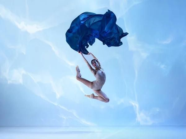 Flying, freedom. flexible ballerina, dancer in high jump with navy fabric over blue background. Art, motion, action, flexibility, inspiration concept. Ballet with silk. Beauty of contemporary dance